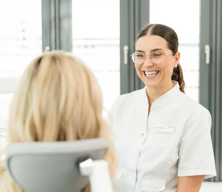 Blick über die Schulter der Patientin auf die lächelnde Zahnärztin