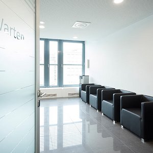Blick an einer Tür vorbei in ein Wartezimmer mit schwarzen Sesseln