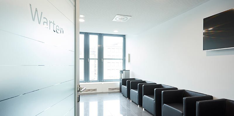 Blick an einer Tür vorbei in ein Wartezimmer mit schwarzen Sesseln