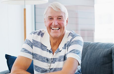 Älterer Herr mit blau-weiß-gestreiften T-Shirt sitzt lächelnd auf einem Sofa
